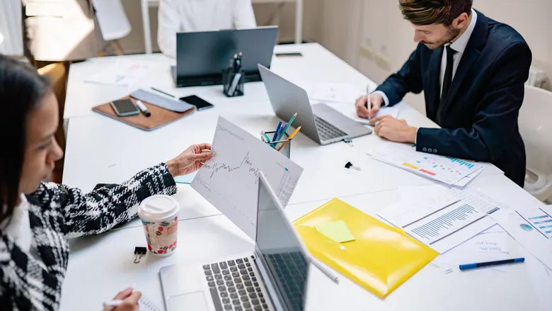 Professionals collaborating in a modern office with laptops and printed documents