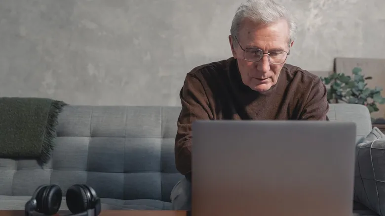 Elderly man sitting on a couch, concentrating on a laptop screen