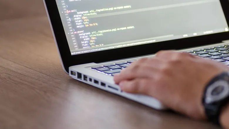 Person coding on a laptop with HTML source code on screen